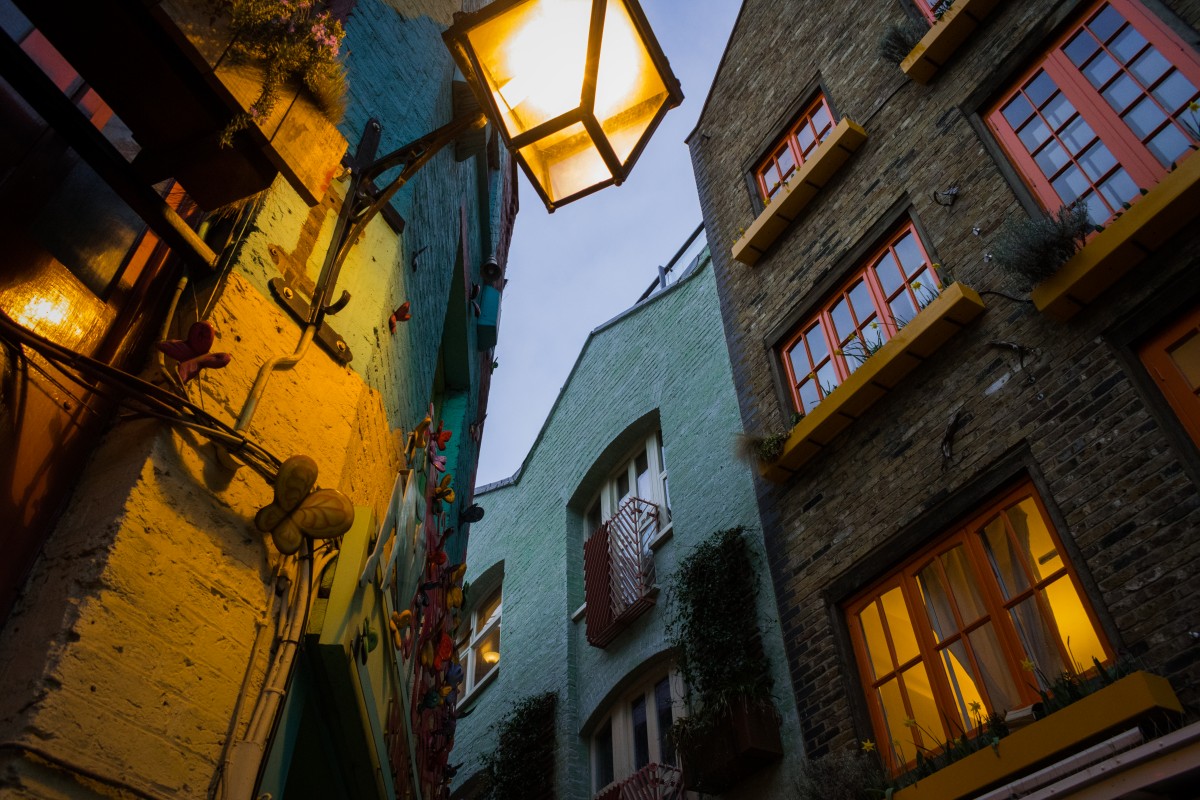 A bottom-up photograph of colorful buildings in a London corner, with a lit electric lamp in the foreground